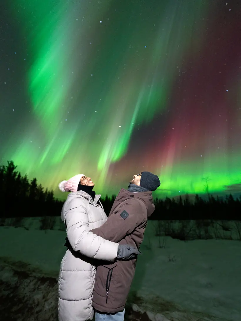 Couple watching green and red northern lights in Rovaniemi