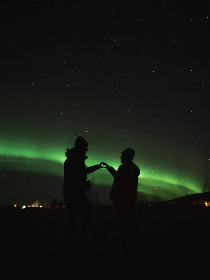 Silhouettes making a heart under the northern lights