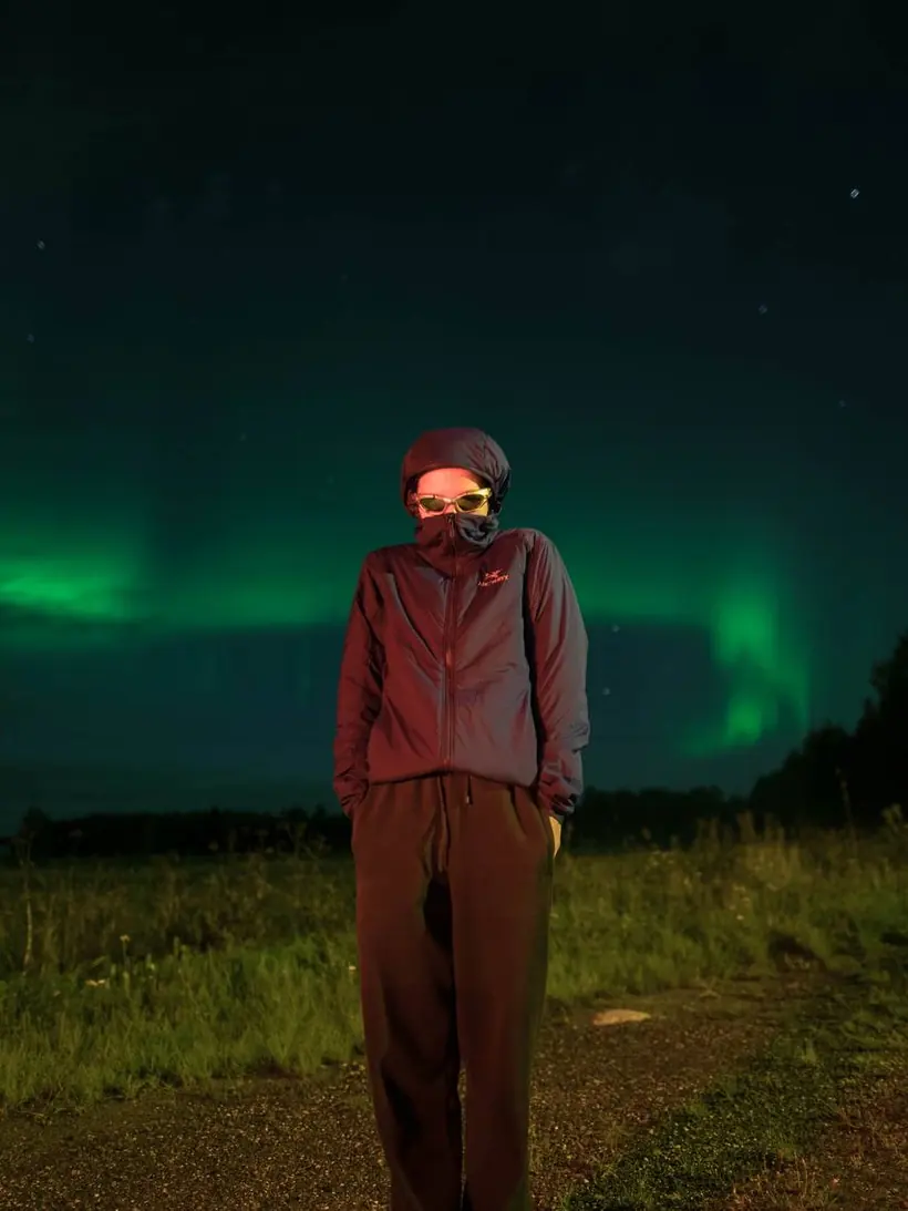 Guest in a hood under a faint green aurora over a summer meadow