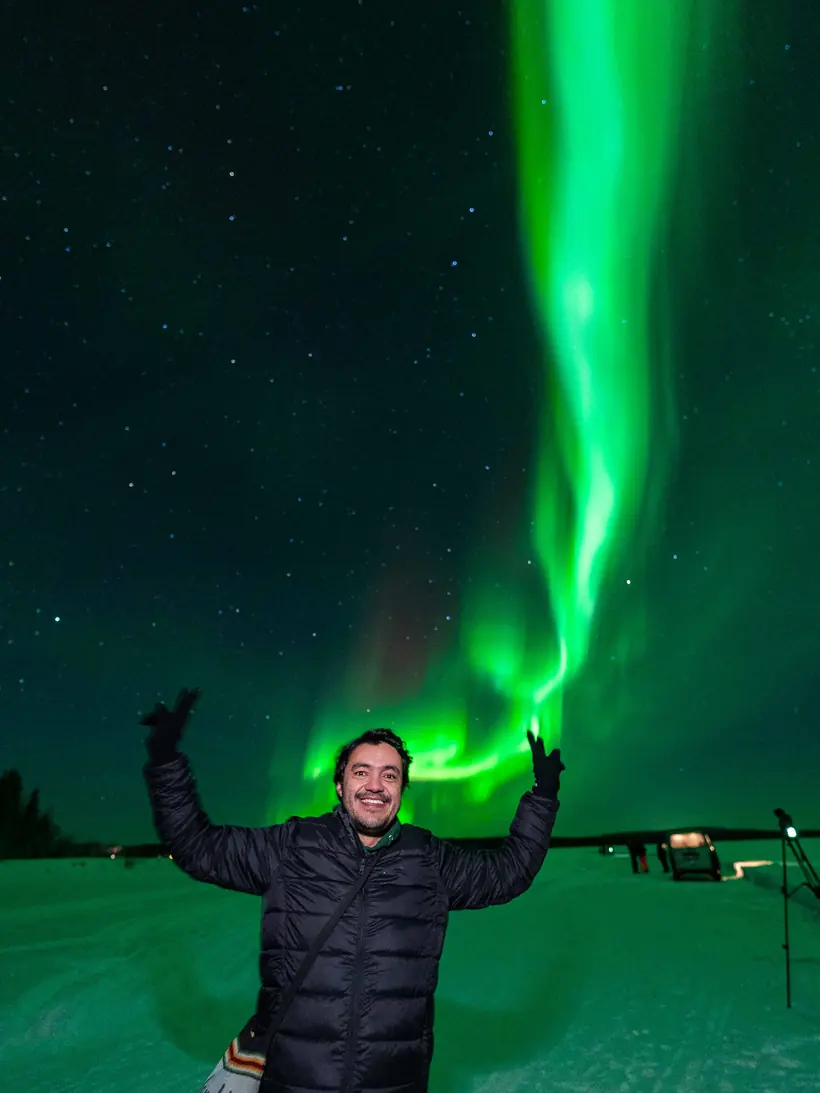 Guest with arms raised beneath a vertical aurora beam
