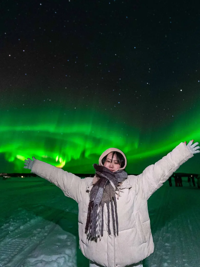 Guest with open arms under a green aurora over a snowy road